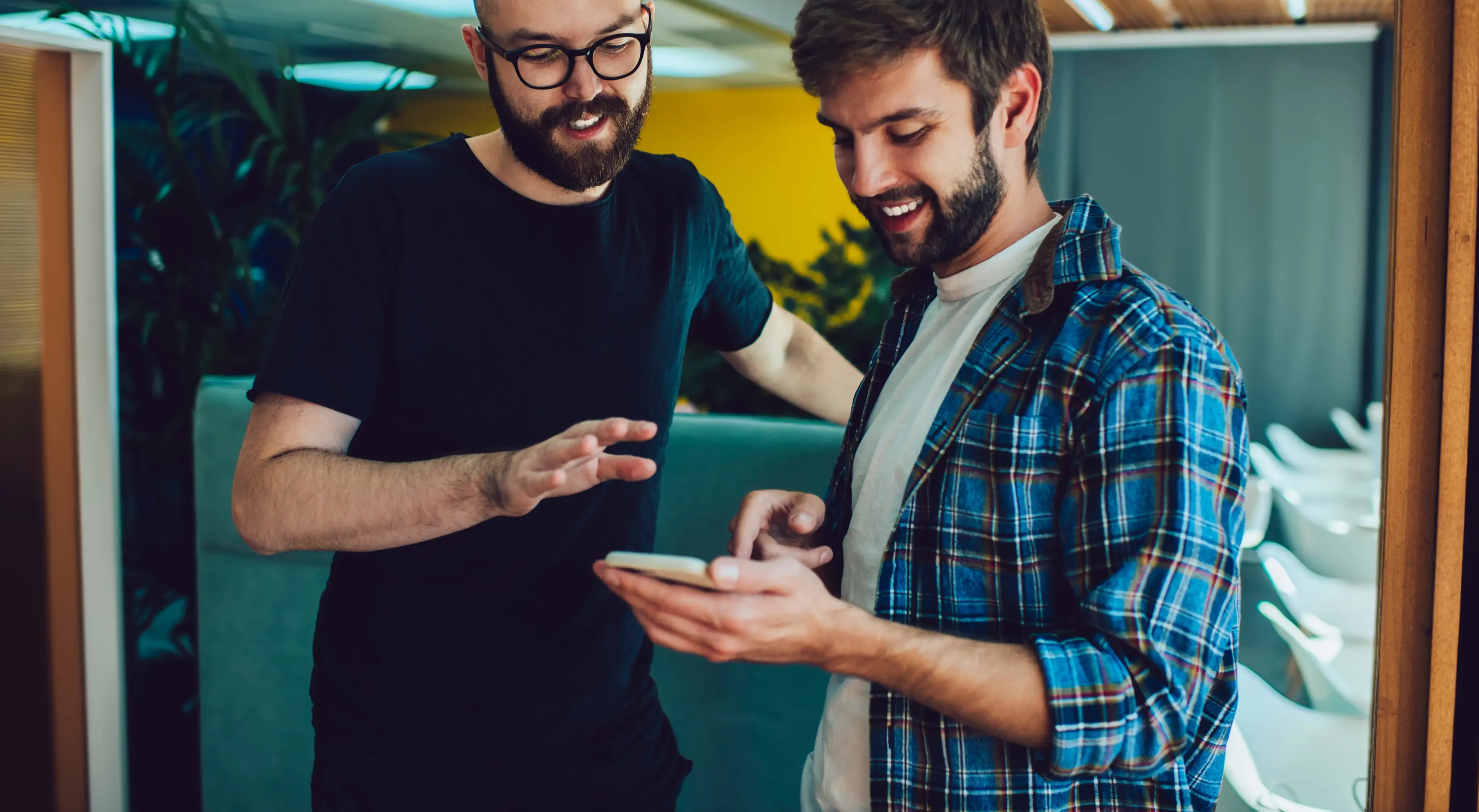 Two people are happily looking at something on a smartphone together in what appears to be an office setting.