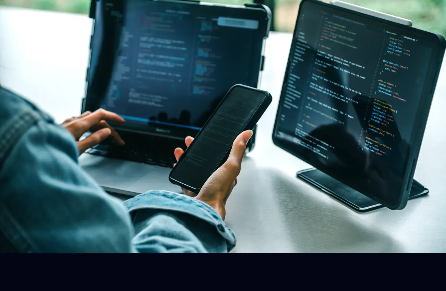A person codes using a tablet, monitor, and smartphone.