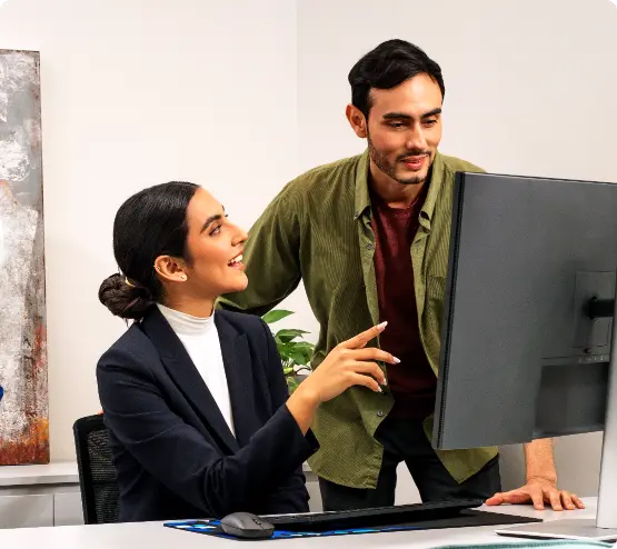 A man and woman in an office are smiling and discussing something on a computer screen.