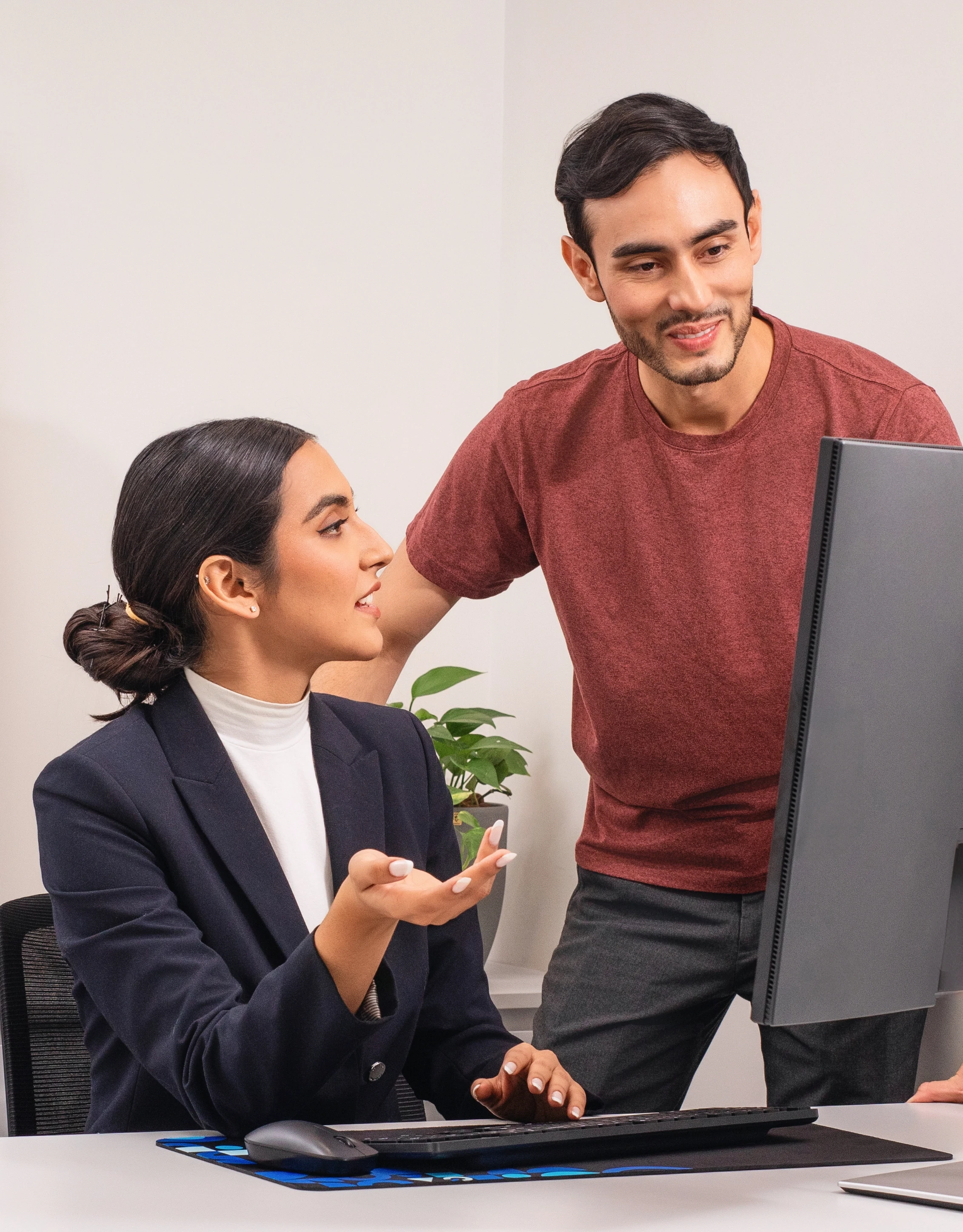 A man and woman in an office are discussing something on a computer screen.